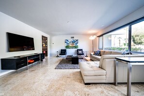 Un salon moderne doté d’un téléviseur à écran plat, d’un canapé, d’une table basse et d’un coin repas avec une table et des chaises.