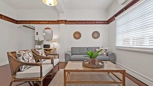 Een woonkamer met een bank, twee fauteuils, een salontafel, een spiegel en een raam met jaloezieën.