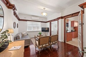 A living room with a sofa, a TV, a dining table with chairs, and a kitchen area with cabinets. - Art Deco in Ascot! ~ 2 Bed / 1 Bath / 1 Car (Ascot)