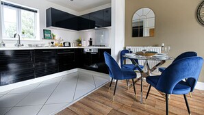 A modern kitchen with black cabinets, a dining area with blue chairs, and a large mirror on the wall. - Luxury Apartment with Balcony, Parking & Fast Wifi (Milton Keynes)