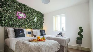 A hotel room with two beds, a green leafy wall, a neon 'hello' sign, and a small potted plant. - Luxury Apartment with Balcony, Parking & Fast Wifi (Milton Keynes)