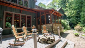 Een houten terras met Adirondack-stoelen en een stenen open haard.
