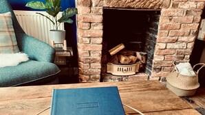 Un salon chaleureux avec une cheminée en briques, un canapé bleu et une table basse en bois sur laquelle est posée une pile de livres.