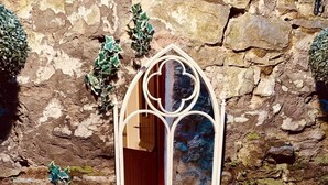 Un mur de pierre avec une porte en bois, un miroir et une table accompagnée de deux fauteuils moelleux.