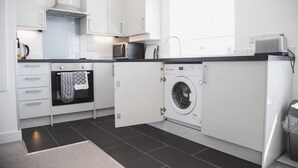 A modern kitchen with white cabinets, a built-in oven, a microwave, a washing machine, and a sink.
