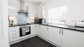 A modern kitchen with white cabinets, a black countertop, a stainless steel range hood, a microwave, a kettle, and a window providing natural light.