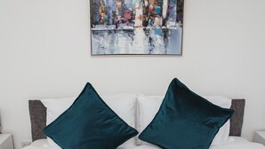 A neatly made bed with two teal pillows and two rolled white towels.
