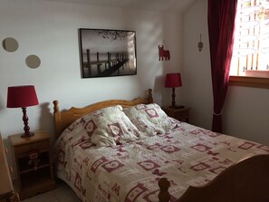 Een slaapkamer met een houten bed, twee nachtkastjes met lampen, een aan de muur hangend schilderij en een raam met gordijnen.