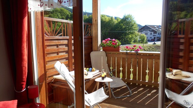 A balcony with a wooden railing, a table with a chair, and a potted plant with flowers. - Apartment with lake view in residence (Gérardmer)
