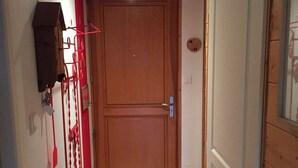 A narrow hallway with a wooden door at the end, a red metal rack with a red mat on the floor, and a white wall with a light fixture. - Apartment with lake view in residence (Gérardmer)