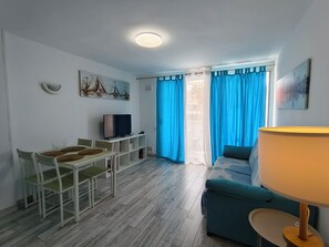 A room with a dining table, chairs, a television, a sofa, and a lamp.