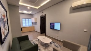 A modern living room with green and beige sofas, a small white table, and a mounted TV displaying a Wi-Fi connection screen. - SOLACE SUITS & HOMES (Abuja)