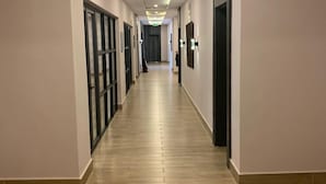 A long, narrow hallway with a wooden floor, recessed ceiling lighting, and doors on both sides. - SOLACE SUITS & HOMES (Abuja)