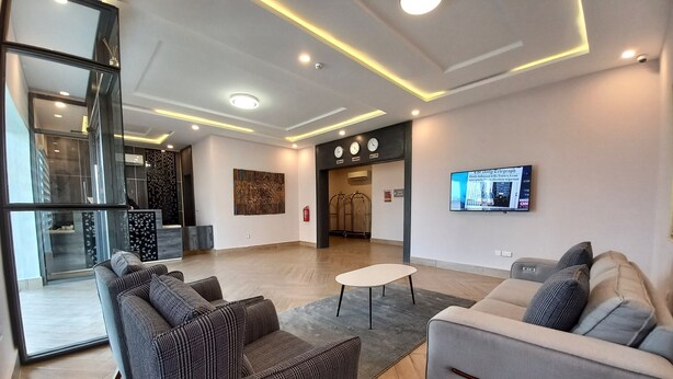 A modern lobby with a reception desk, seating area, and a mounted TV. - SOLACE SUITS & HOMES (Abuja)