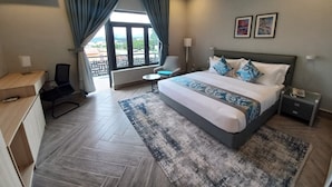 A hotel room with a bed, a desk, a chair, a small table, a nightstand, and a window with curtains. - SOLACE SUITS & HOMES (Abuja)