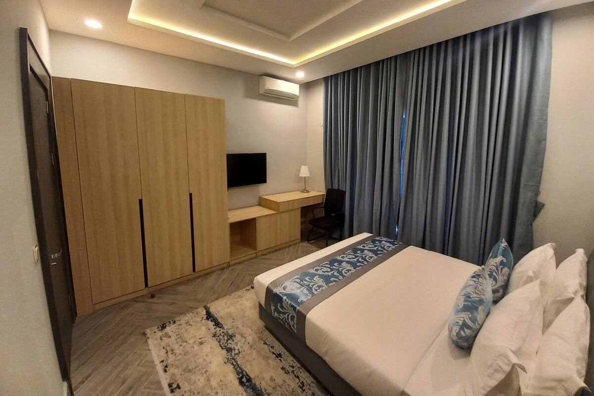 A modern hotel room with a large bed, a desk, a TV, and a wardrobe.