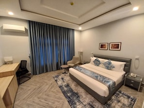 A modern hotel room with a large bed, a desk, a chair, and a small table. - SOLACE SUITS & HOMES (Abuja)