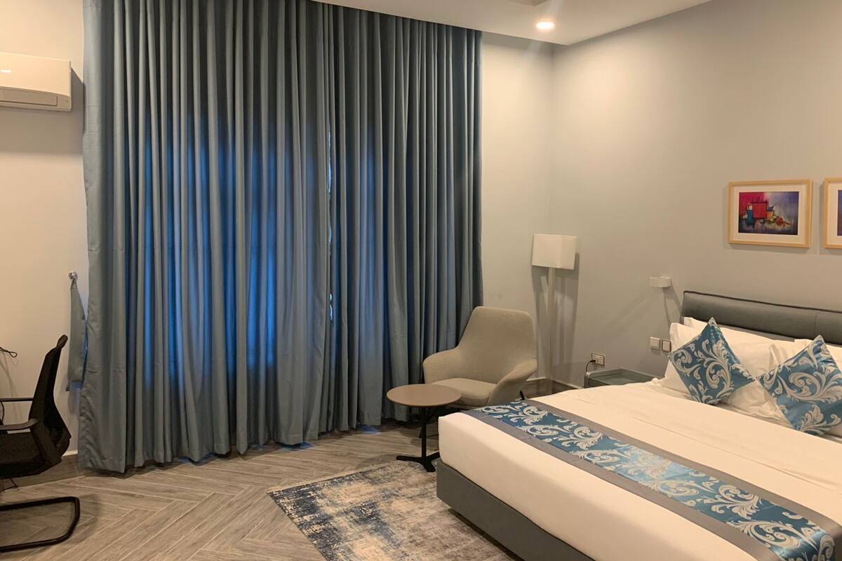 A hotel room with a bed, a chair, a desk, and a large window with curtains.