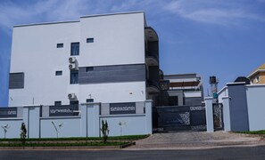 A modern building with a flat facade, multiple air conditioning units, and a gated entrance. - SOLACE SUITS & HOMES (Abuja)