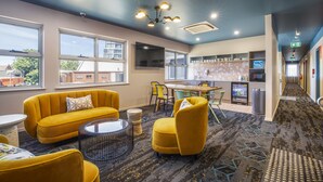 Un rebedor d'hotel modern amb sofàs grocs, una taula de cafè rodona i una zona de cuina amb nevera i microones.