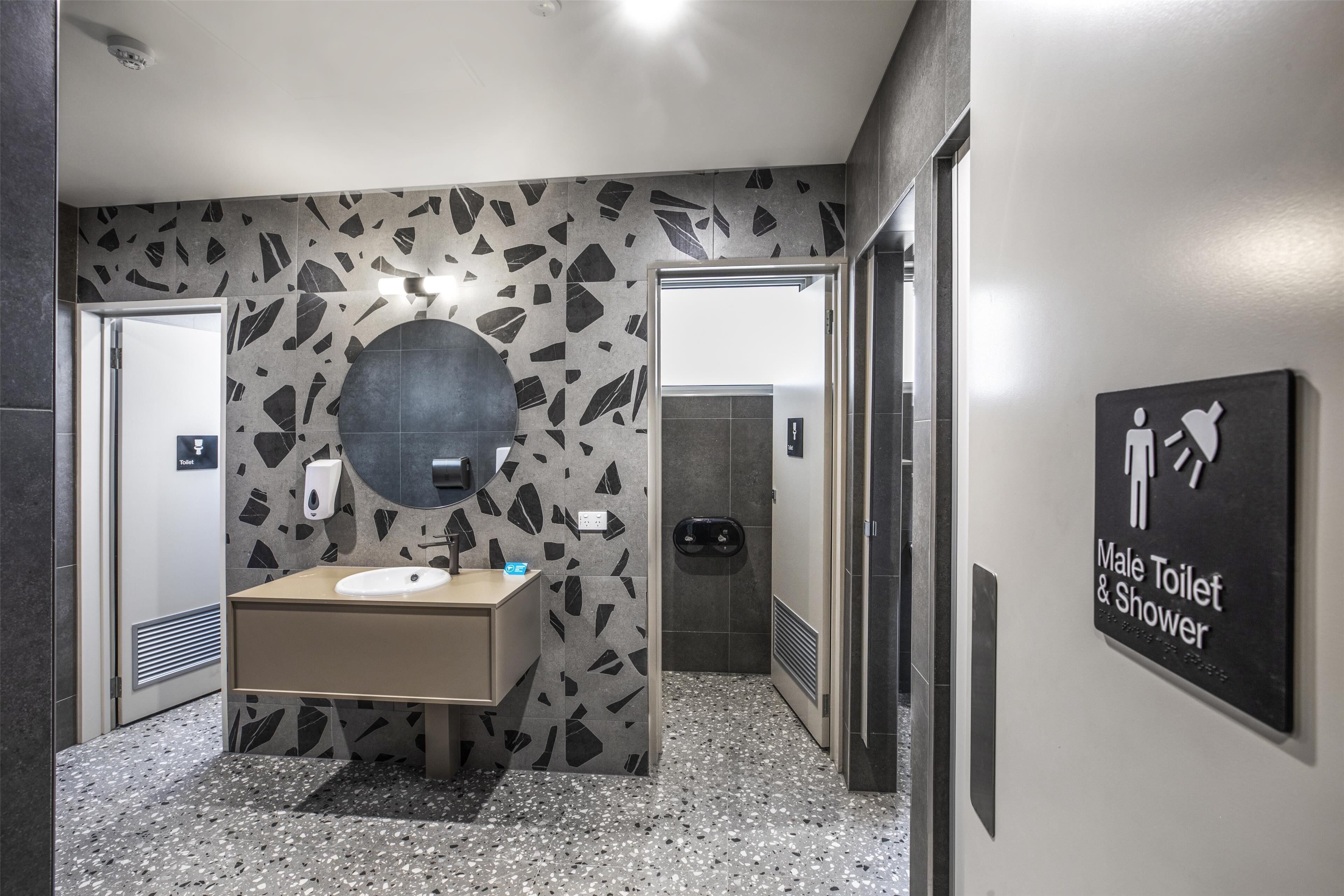 Un baño moderno para hombres con un revestimiento de pared con diseño de granito, un lavamanos y un letrero que indica las instalaciones.