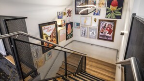 Una escala amb barana metàl·lica, envoltada d'obres d'art diverses emmarcades a les parets.