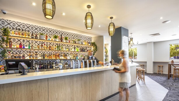 Zona de bar amb taulell, estanteries plenes de botelles i llums penjants.