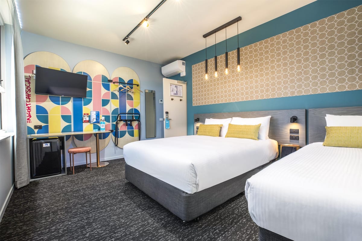 A hotel room with two beds, a desk, and a TV.
