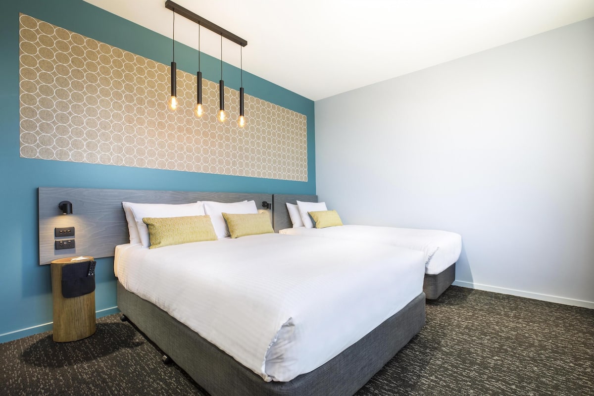 A modern hotel room with a large bed, a wall-mounted light fixture, and a small bedside table.