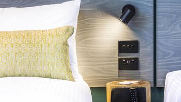 Habitación de hotel con cama, mesita de noche con control remoto, lámpara de pared y enchufe.