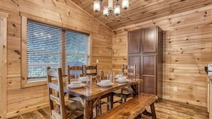 Une pièce aux murs lambrissés, avec une table à manger dressée pour quatre personnes, un banc et un lustre.