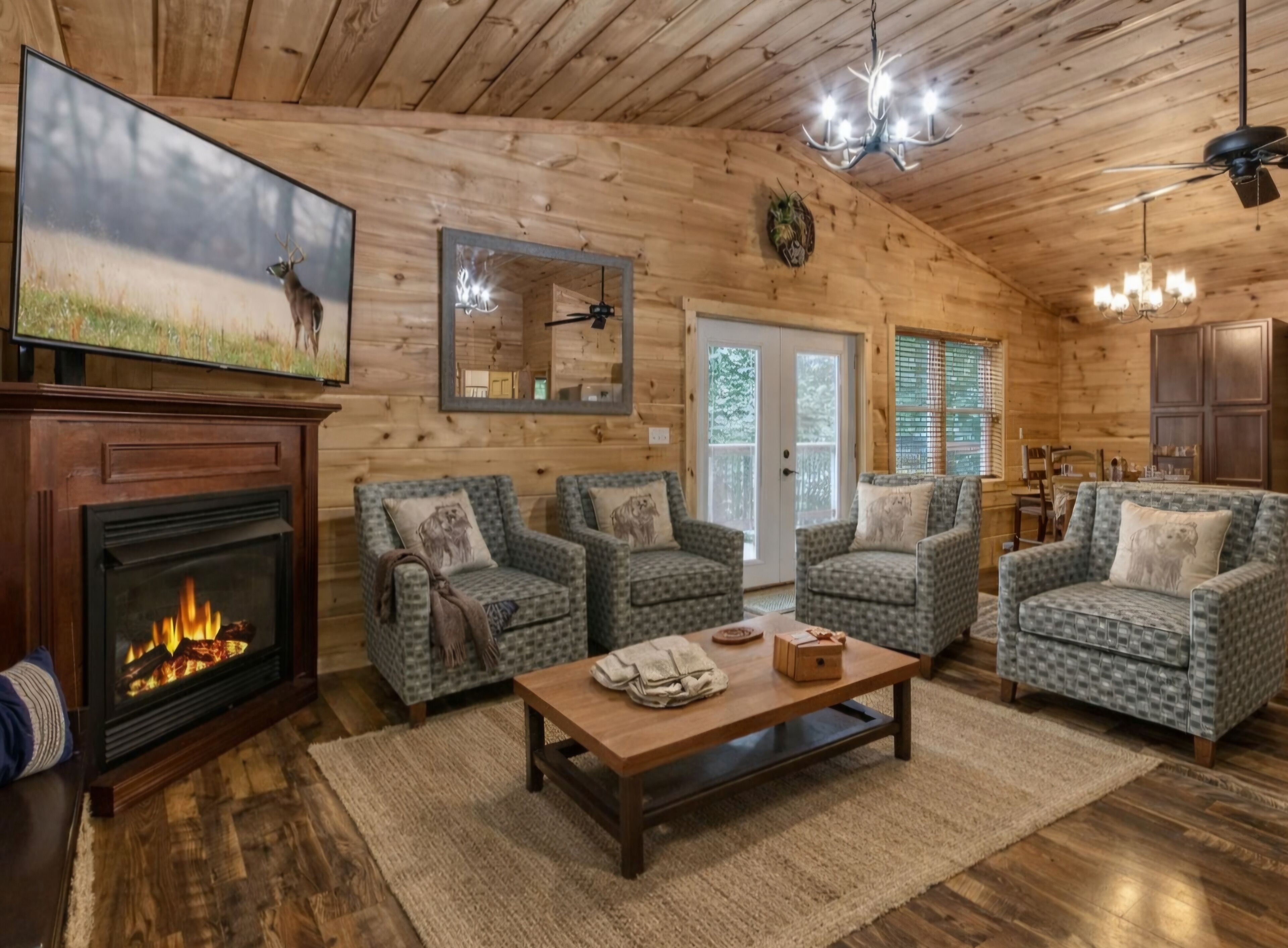 Un interior de cabaña acogedor con chimenea, sillones estampados, techo de madera y un televisor montado en la pared.