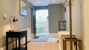 A hallway with a desk, a lamp, a coat rack, and a view of the outside. - The Garden Flat - An Elegant Georgian Single Level Holiday Home (Charmouth)