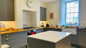 A modern kitchen with grey cabinets, a central island, a stove, a sink, and a window providing natural light. - The Garden Flat - An Elegant Georgian Single Level Holiday Home (Charmouth)