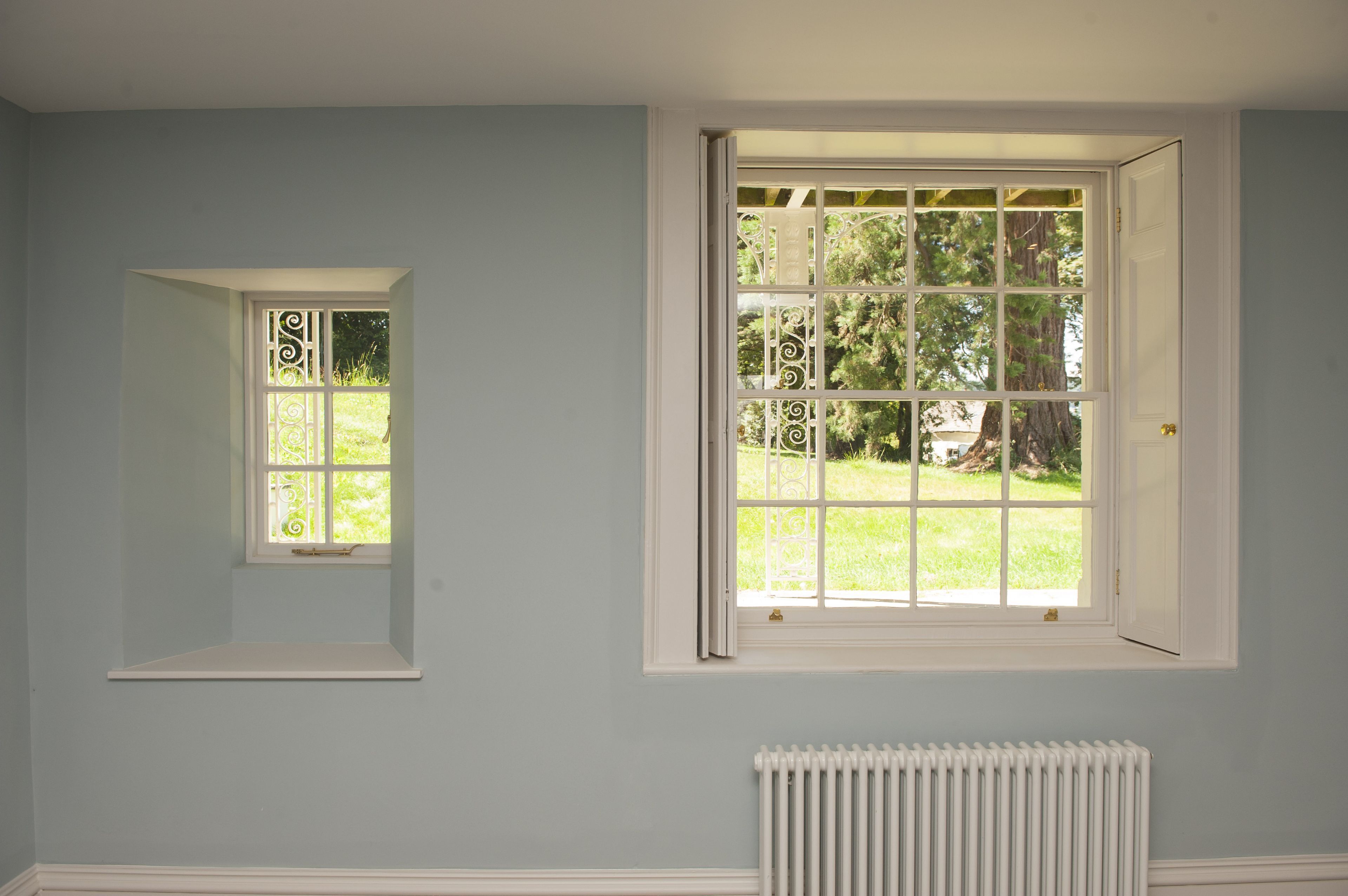 Ein Zimmer mit einem großen Fenster, einem kleineren Fenster und einer Heizung.