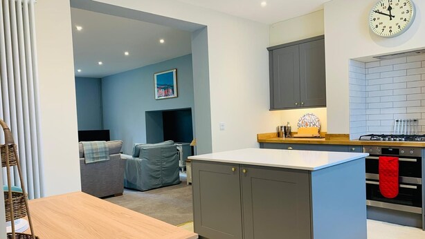 A modern kitchen with grey cabinets, a white countertop, and a red oven towel. - The Garden Flat - An Elegant Georgian Single Level Holiday Home (Charmouth)