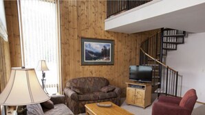 Una sala de estar con sofá, sillón y televisor sobre un mueble de madera.