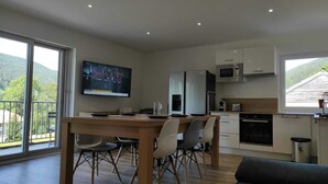 A modern kitchen with a dining area, large windows, and a TV. - LELEXINE APARTMENT AT THE FOOT OF THE MONTS JURA SLOPES (LELEX)