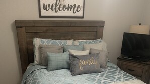 Una camera da letto con un letto, cuscini, un cartello con la scritta 'welcome', una televisione e un comodino.
