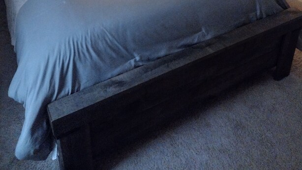 Camera da letto con un letto, cuscini, un comodino, una lampada e una TV che mostra una selezione di film.