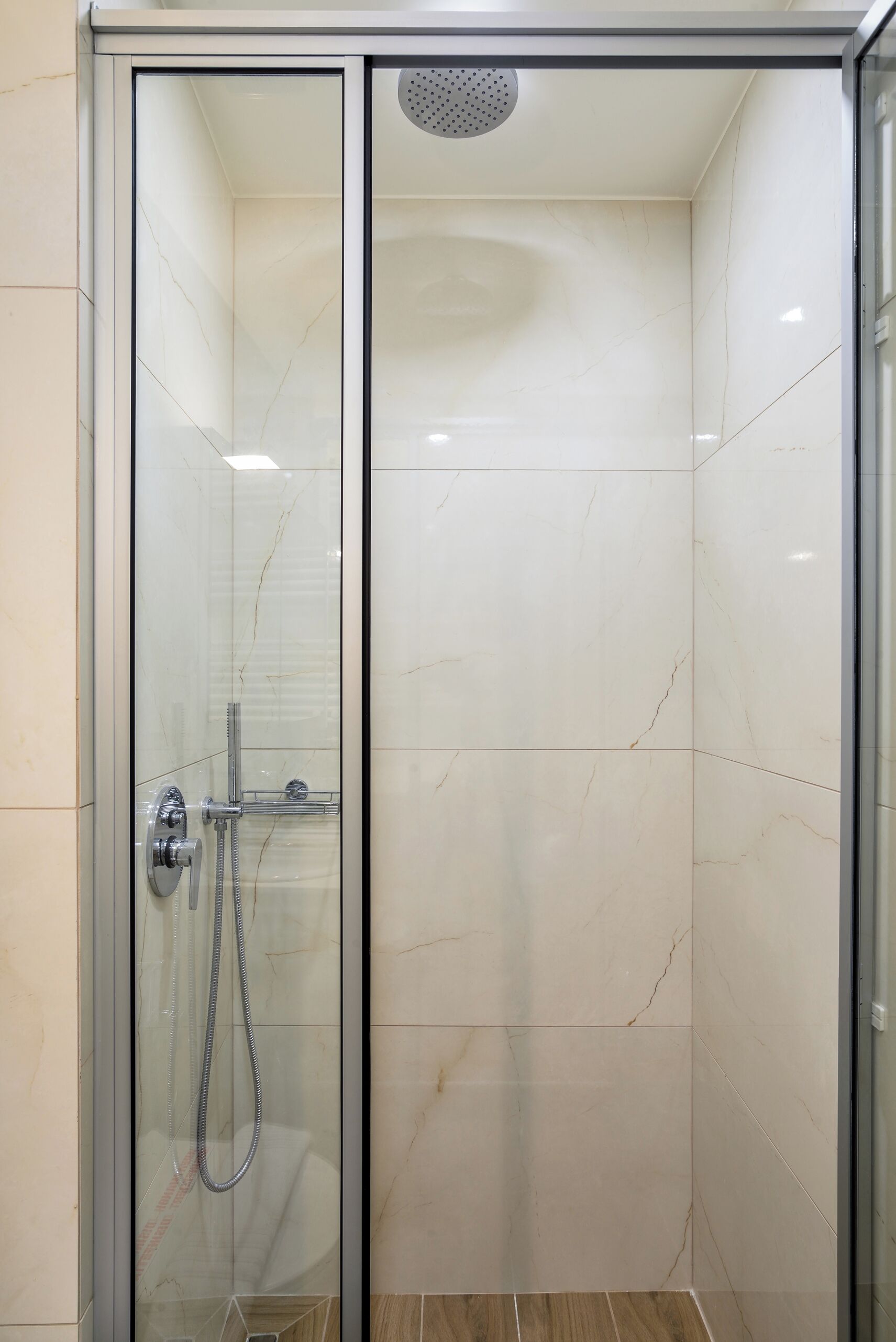 A glass-enclosed shower stall with a handheld showerhead and a wall-mounted faucet.