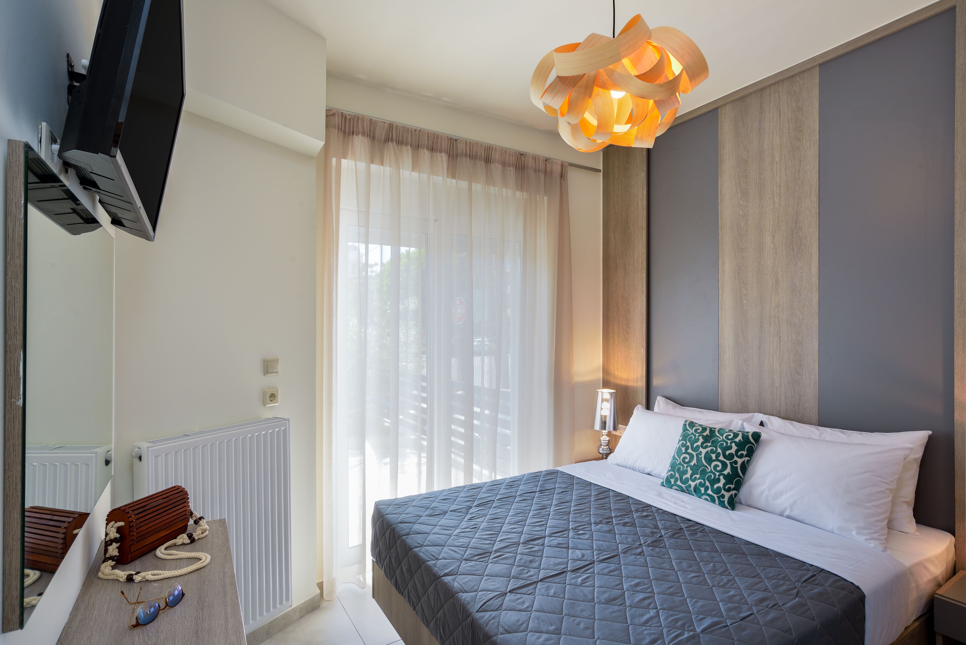 A modern bedroom with a large bed, a TV mounted on the wall, a radiator, and a unique pendant light.