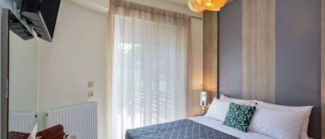 A modern bedroom with a large bed, a TV mounted on the wall, a radiator, and a unique pendant light.