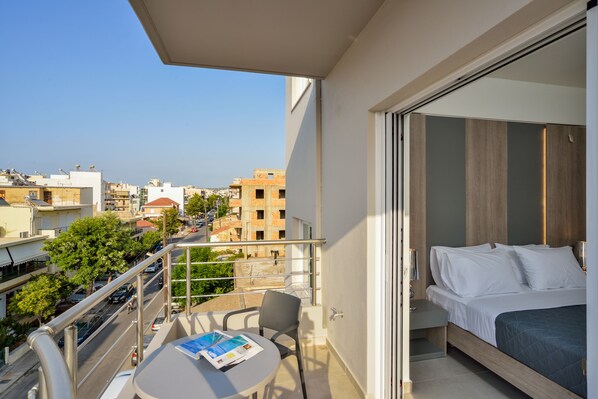 A balcony with a bed, a table with a magazine, and a view of the cityscape.