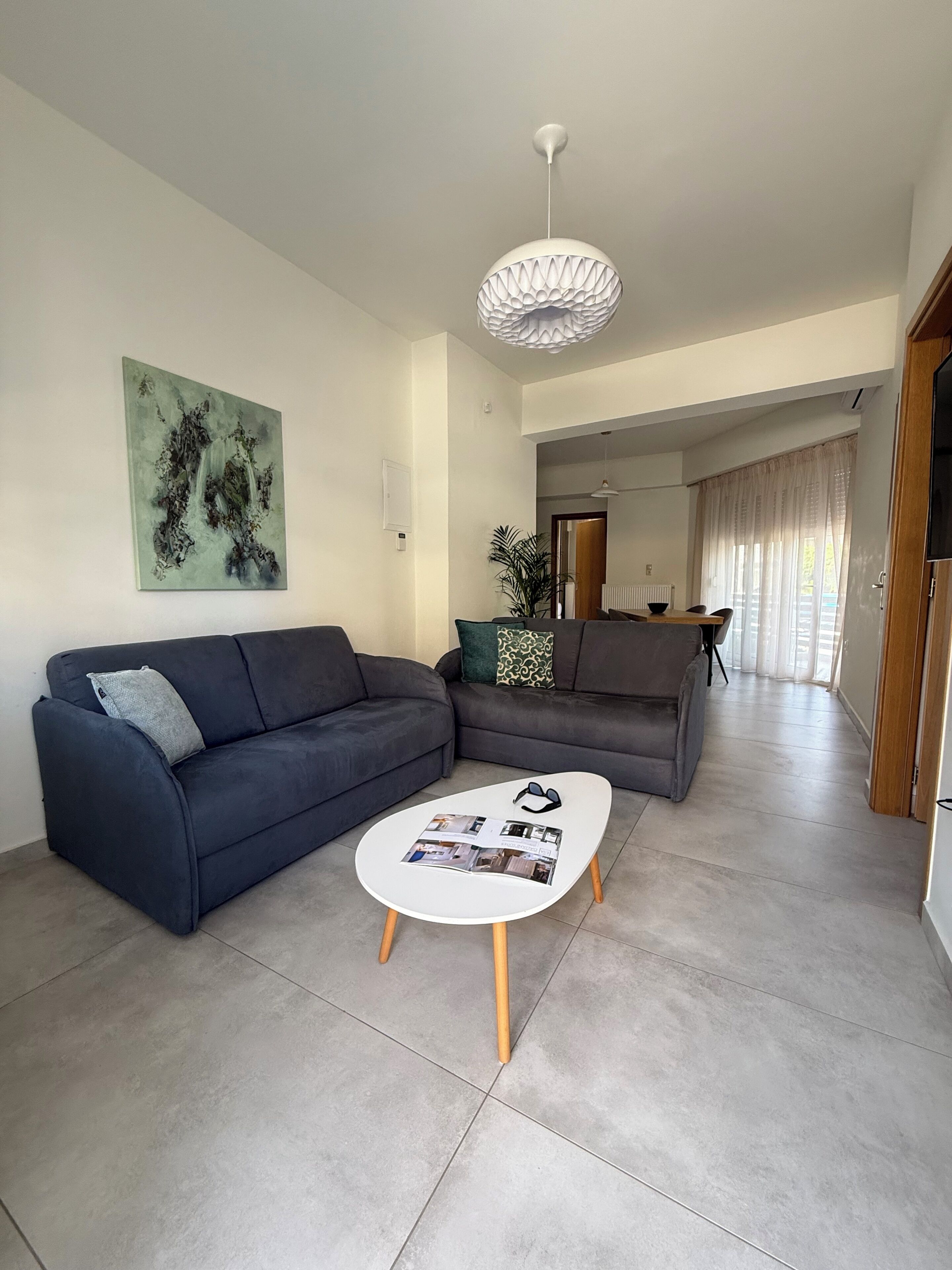 Una sala de estar moderna con un sofá azul oscuro, una mesa de centro blanca y una lámpara de techo original.