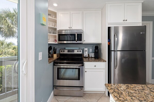 A compact kitchen with white cabinets, a stainless steel refrigerator, a microwave, an oven, and a stove.