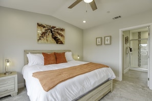 A bedroom with a bed, nightstands, a ceiling fan, a painting, and a shower area.