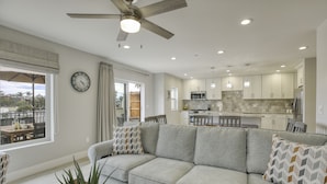 Un soggiorno moderno con un divano grigio, una ventola a soffitto e vista sulla cucina.