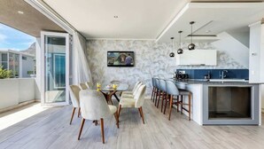 A modern kitchen with a large island, a dining area with a round table and chairs, and a large window overlooking a balcony.