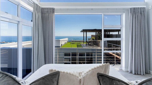 A modern hotel room with a large balcony, a view of the sea, and a pool area.